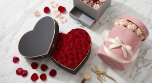 An arranged flat-lay composition of diverse custom flower gift boxes on a light marble surface. Features open magnetic heart boxes, round hat boxes with silk ribbon, and square rigid boxes.
