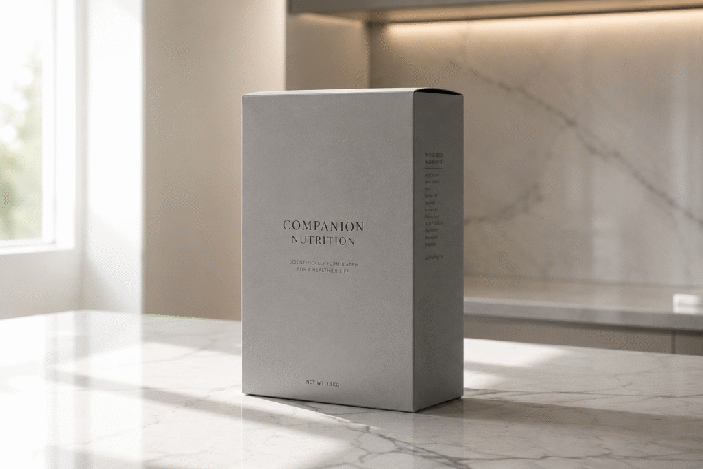 A pristine, sharp-edged matte grey premium folding carton for pet supplements, standing upright on a luxurious white marble kitchen countertop bathed in soft morning sunlight, replacing cheap plastic pouches.