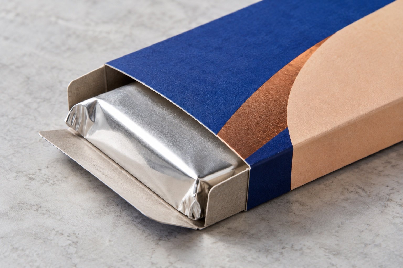 Concept close-up of a printed blue and apricot folding carton holding a sealed silver-wrapped chocolate bar