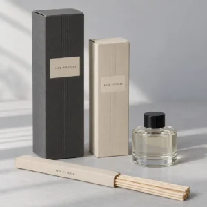 Illustrative charcoal and ivory reed diffuser cartons with a capped glass bottle and separate paper reed sleeve
